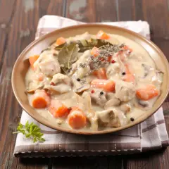 Un plat de blanquette de veau crémeuse avec des carottes et des champignons, garni de thym et de feuilles de laurier.