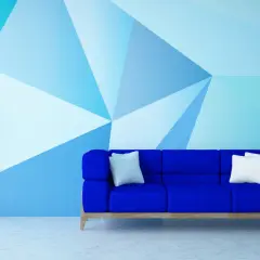 Niebieska sofa i roślina w donicy na tle ściany z geometrycznym wzorem, tworzącym efekt malarski.