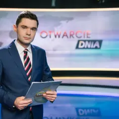 Jan Niedziałek, dziennikarz w garniturze, trzyma dokumenty w studiu telewizyjnym z napisem "OTWARCIE DNIA".