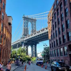 Ulica w **brooklyn** z ceglanymi kamienicami i majestatycznym mostem w tle.