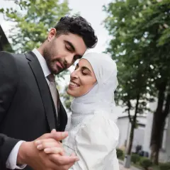 Un uomo in abito scuro e una donna con velo bianco si abbracciano teneramente, celebrando il loro matrimonio misto.