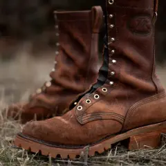 Two brown leather work boots with a lug sole, meaning a thick, rugged sole with deep treads for excellent grip, stand in dry grass.