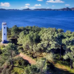 El faro de Cabo Home se alza solitario en una colina verde, vigilando el azul intenso del mar y las islas lejanas.
