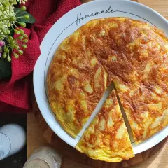 A golden-brown potato frittata with a slice cut out, on a white plate with "Homemade" written on it.