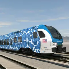 Nowoczesny pociąg Stadler FLIRT H2 z niebiesko-białym wzorem pędzi po torach.