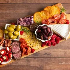 Un invitante tagliere salumi e formaggi con olive, lamponi, pane tostato e vari salumi.