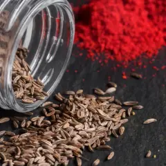 Braune Kümmelsamen quellen aus einem Glas, daneben leuchtend rote und gelbe Gewürzpulver. Was ist Cumin? Es ist dieses aromatische Gewürz!