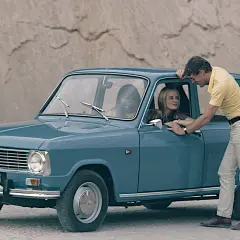 En man lutar sig mot en blå Renault 6, en av många gamla Renault-modeller, medan en kvinna sitter bakom ratten.