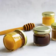 Małe słoiczki z miodem, jeden leży, obok drewniana chochla. Kremowany miód wady? Nie widać żadnych.