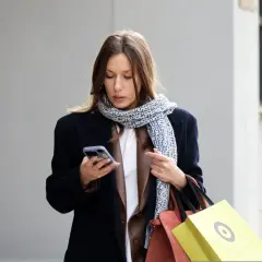 Kobieta w granatowym płaszczu i wzorzystym szaliku trzyma telefon. Czyżby szukała informacji, jaki kolor jest teraz modny?