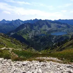 Widok z przełęczy na skraju Orlej Perci na Tatry Wysokie. Dwa jeziora w dolinie, skaliste zbocza i szczyty w oddali.