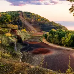 Paisaje del parc natural de la zona volcànica de la Garrotxa con laderas escalonadas, vegetación otoñal y el cielo rosado del atardecer.