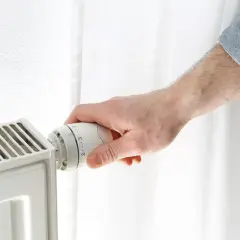 Dłoń reguluje termostat grzejnika, próbując obniżyć zbyt wysoką temperaturę w domu.
