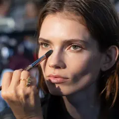 Maquillista aplica sombra en el párpado de una modelo, creando combinaciones sombra delineador ojos perfectas.