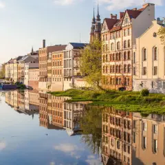 Nad rzeką w najmniejszym województwie w Polsce, w słoneczny dzień, odbijają się w wodzie zabytkowe kamienice.