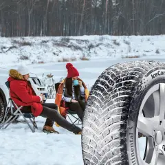 Ett par njuter av en paus i snön bredvid en bil, med en vinterdäck i förgrunden. Välj dubb eller dubbfritt för din trygghet.