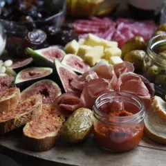 Leckere Zutaten für **Tapas selber machen**: Feigen, Schinken, Oliven, Brot und Dips auf einem rustikalen Brett.