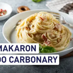 Pyszny makaron do carbonary z boczkiem i kremowym sosem, podany w białej misce. Obok przyprawy i liść bazylii.