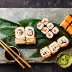 Sushi-Platte mit Lachs-Rollen, Nigiri und Beilagen. So isst man Sushi richtig: mit Stäbchen, Sojasauce, Wasabi und eingelegtem Ingwer.
