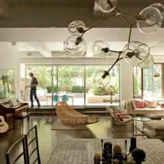 A man walks through a modern living room, captured in this interior architecture photography. A piano, guitar, and unique light fixture are visible.