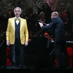 Andrea Bocelli w Polsce, w złotym fraku, śpiewa pod batutą dyrygenta.