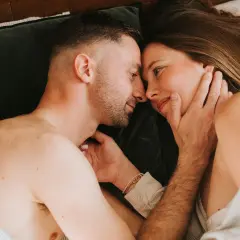 Un couple se regarde tendrement au lit. Ils semblent se retrouver après une période difficile, peut-être après une naissance et une épisiotomie, redécouvrant l'intimité.