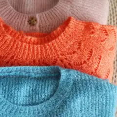 Drei gestapelte Pullover in Rosa, Orange und Blau. Die feine Lammwolle ist bereit für das Waschen, um ihre Weichheit zu erhalten.