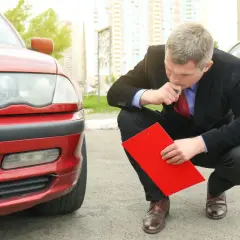 Man i kostym inspekterar en röd bil med en röd pärm, kanske för en digital servicebok.