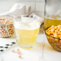 Płyn z ciecierzycy, czyli aquafaba, w szklance i dzbanku, obok miski z ziarnami. To wegański zamiennik jajek.