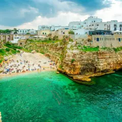 Malownicza plaża Polignano a Mare z turkusową wodą, skalistymi klifami i białymi budynkami na szczycie.
