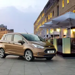 Brązowy Ford B-Max na tle miejskiej zabudowy. Idealny do miasta, jego wymiary sprawiają, że parkowanie to przyjemność.