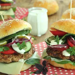Dwa domowe burgery z serem, warzywami i sosem na drewnianym tle.