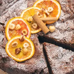 Torta di pane ricetta della nonna, cosparsa di zucchero a velo, decorata con fette d'arancia, nocciole e cannella.