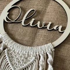 Un bel attrape-rêve personnalisé pour fabriquer un attrape rêve avec prénom. Le prénom "Olivia" est inscrit en lettres de bois sur un cercle orné de macramé.