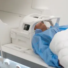 Pacjent leży w aparacie do rezonansu głowy, otulony kocem.