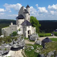 Zamek na skale w krajobrazie Jury Krakowsko-Częstochowskiej. W tle las i błękitne niebo z chmurami.