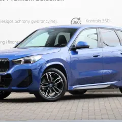 Niebieskie BMW iX1 na tle białej ściany z informacjami o gwarancji i finansowaniu. Sprawdź atrakcyjną bmw ix1 cena!