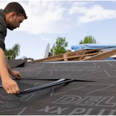 Dekarz układa membranę na dachu. Zastanawiasz się, ile kosztuje godzina pracy dekarza?