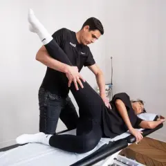 Un kinésithérapeute guide un exercice kiné hanche, soulevant la jambe d'une patiente allongée sur une table de massage.