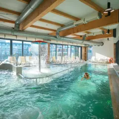 Relaks w aquaparku w Międzyzdrojach. Kobieta pływa w basenie z wodospadem i leżakami.