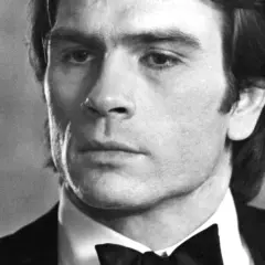 Młody Tommy Lee Jones w czarnym smokingu z muszką, zamyślony.