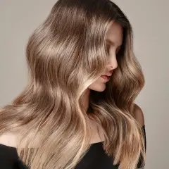 Mujer con cabello largo y ondulado en tonos castaños y rubios, ideal para quienes buscan cómo quitar el tinte del cabello y dejarlo natural.