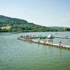 Ludzie odpoczywają na drewnianych pomostach nad jeziorami Dolnego Śląska. W tle zielone wzgórza.