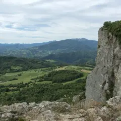 Vista panoramica dalla cima della Pietra di Bismantova, con colline verdi e montagne all'orizzonte sotto un cielo nuvoloso.