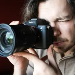 Mężczyzna zamyka oko, patrząc przez wizjer aparatu Sony Alpha 7. Premiera Sony a7 IV budzi emocje.