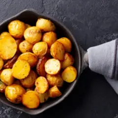 Patatas doradas y tiernas listas para cocer, con romero fresco en una sartén de hierro fundido.