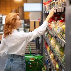 Kobieta w białej koszuli wybiera produkty FMCG, czyli szybko zbywalne towary, w supermarkecie.