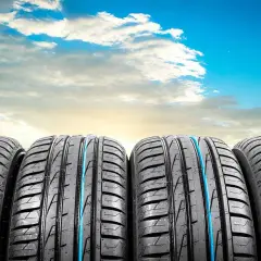 Quatre pneus de voiture, parfaits pour l'été ou toutes saisons, alignés sous un ciel bleu éclatant avec des nuages blancs.