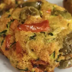 Polpette di zucchine dorate e saporite, con pomodorini e olive verdi, pronte per essere gustate.