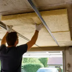 Un homme installe des panneaux isolants sur le plafond de son garage pour une meilleure isolation.